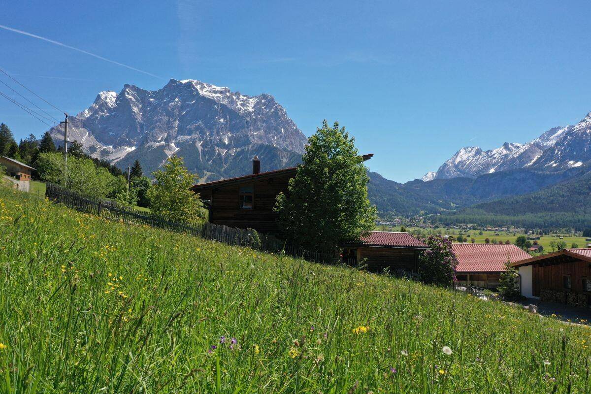 Idyllisches Holzhaus auf einem grünen Hügel mit weitem Blick auf die schneebedeckten Berge.