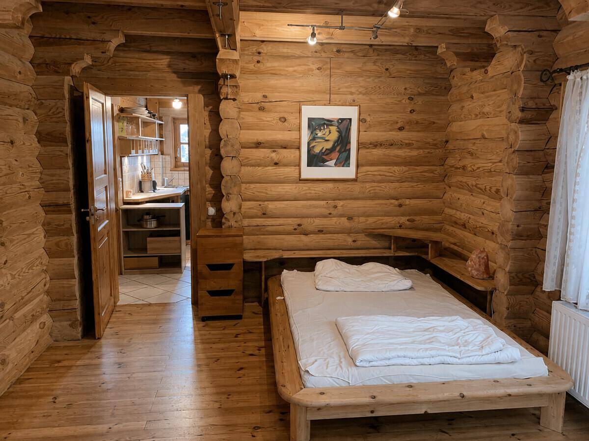 Gemütliches Schlafzimmer mit Holzwänden, Einzelbett und Blick auf die angrenzende Küche.