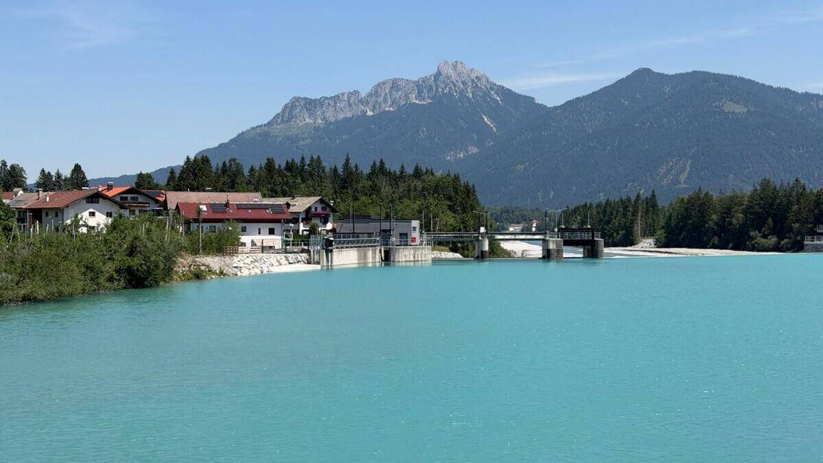Türkisfarbener Fluss vor einer beeindruckenden Bergkulisse unter blauem Himmel.