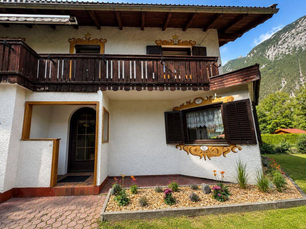 Eingangsbereich des Hauses mit Holzbalkon und traditioneller Fassadengestaltung, umgeben von Grün.