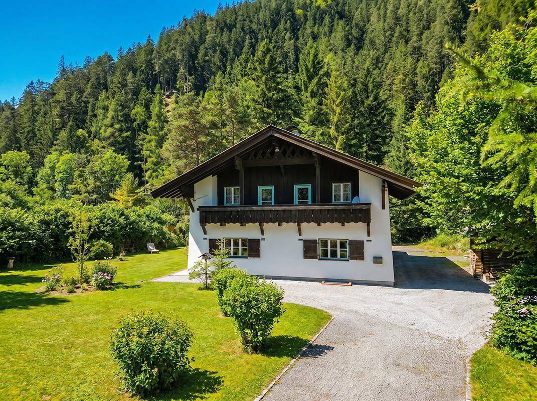 Traditionelles Haus mit Holzbalkon, umgeben von einem weitläufigen Garten und Waldlandschaft.