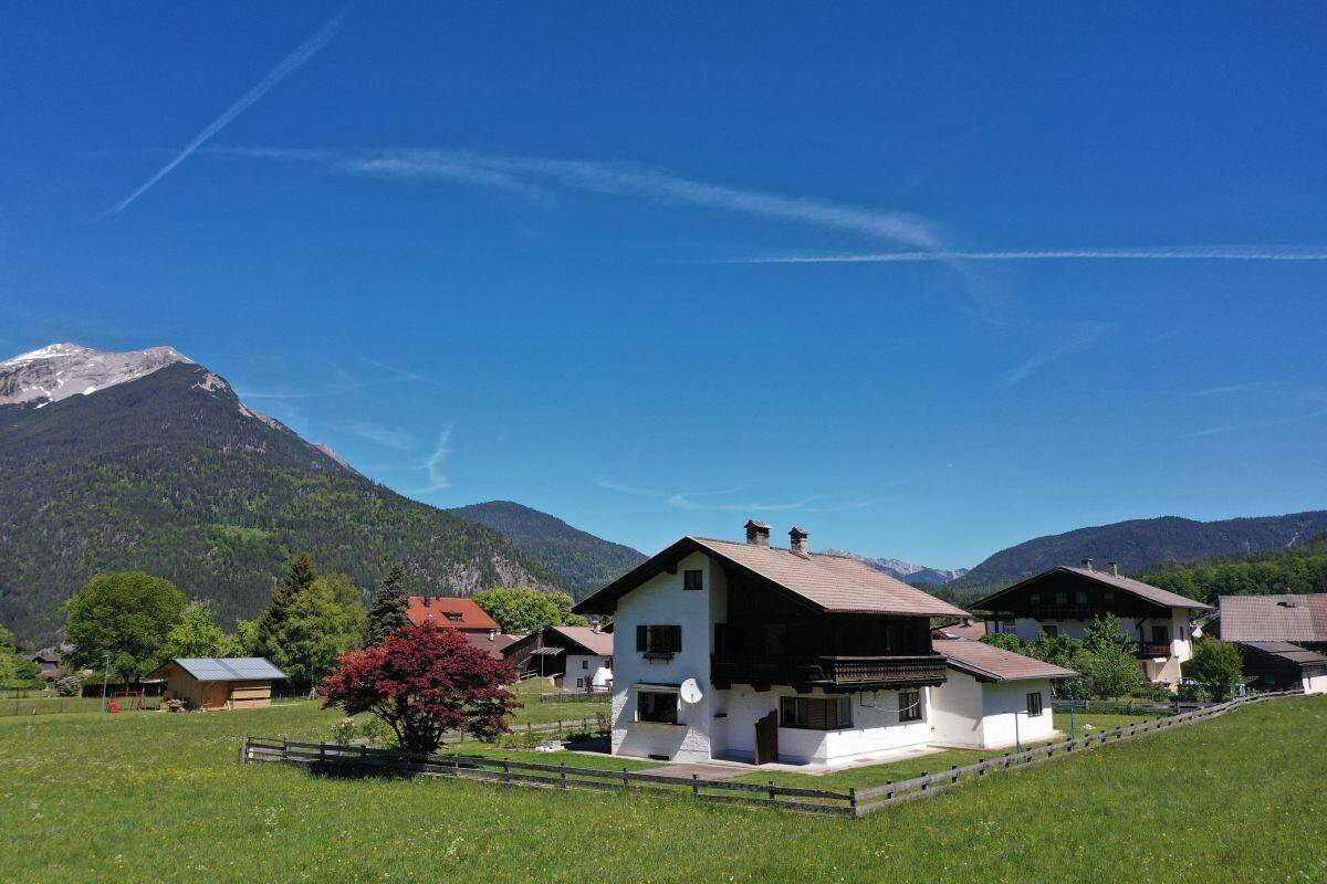 Alpines Haus mit traditioneller Architektur, umgeben von Wiesen und einer beeindruckenden Bergkulisse.