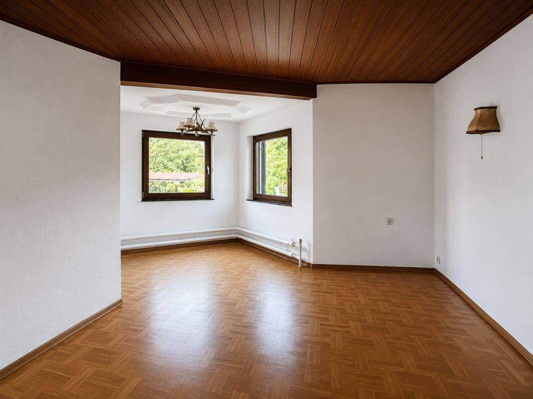 Heller Wohnbereich mit Holzparkettboden und Holztäfelung an der Decke, mit Blick ins Grüne.