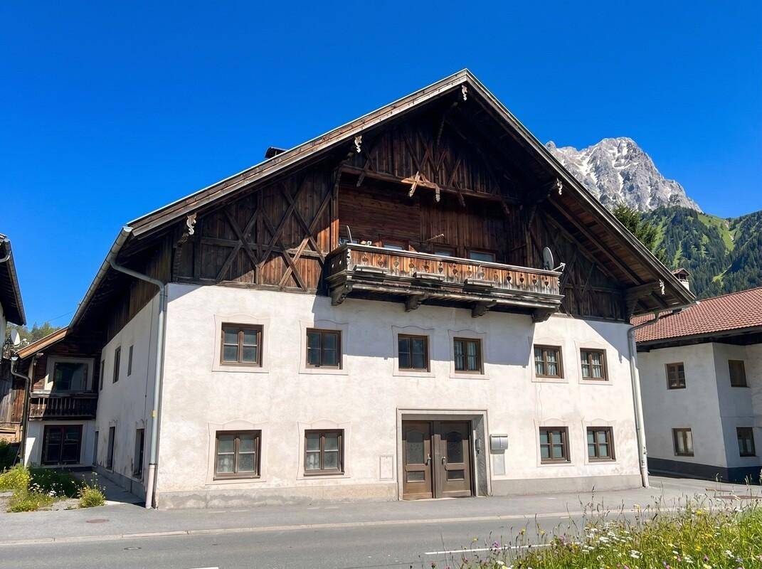 Traditionelles alpines Gebäude mit weißer Fassade und Holzbalkonen vor einer beeindruckenden Bergkulisse.