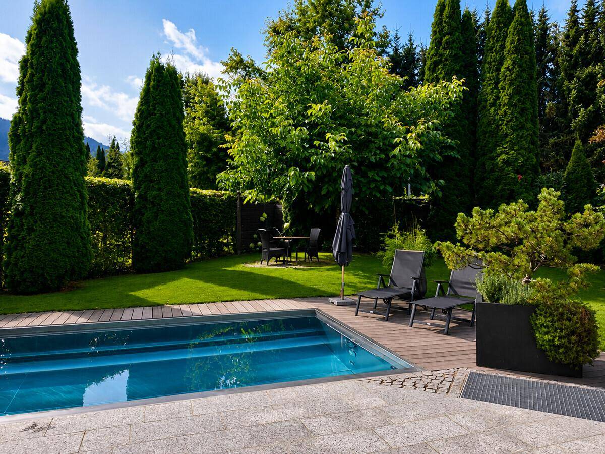 Ruhiger Garten mit Pool, Holzdeck und üppiger Bepflanzung unter strahlendem Sonnenschein.