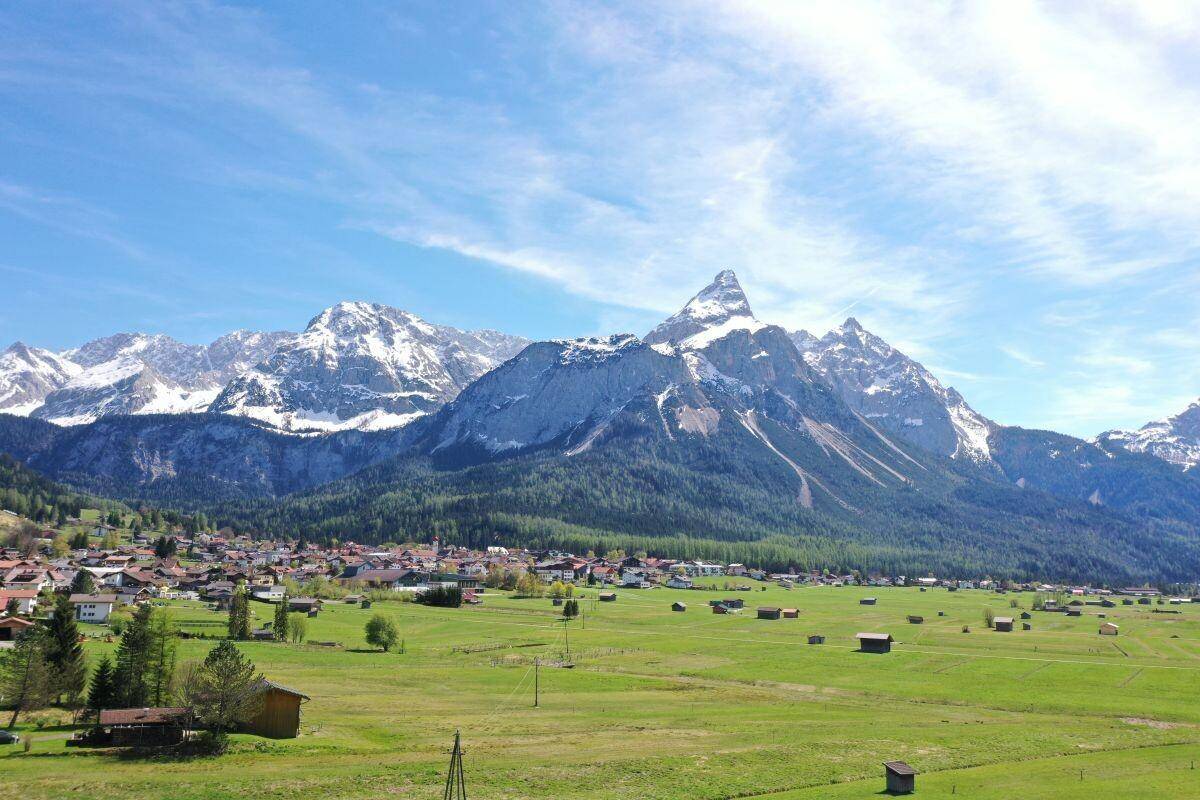 Panoramablick auf ein malerisches Dorf in einem grünen Tal, umgeben von majestätischen schneebedeckten Bergen.