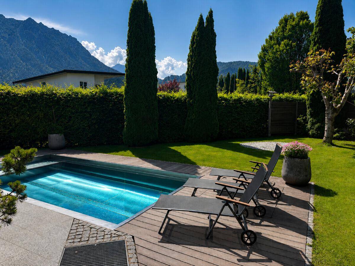 Entspannender Poolbereich im Garten mit Liegestühlen und malerischem Bergblick.