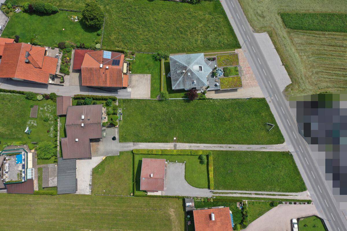 Luftaufnahme einer Wohnsiedlung mit mehreren Grundstücken, Häusern und einer angrenzenden Straße.
