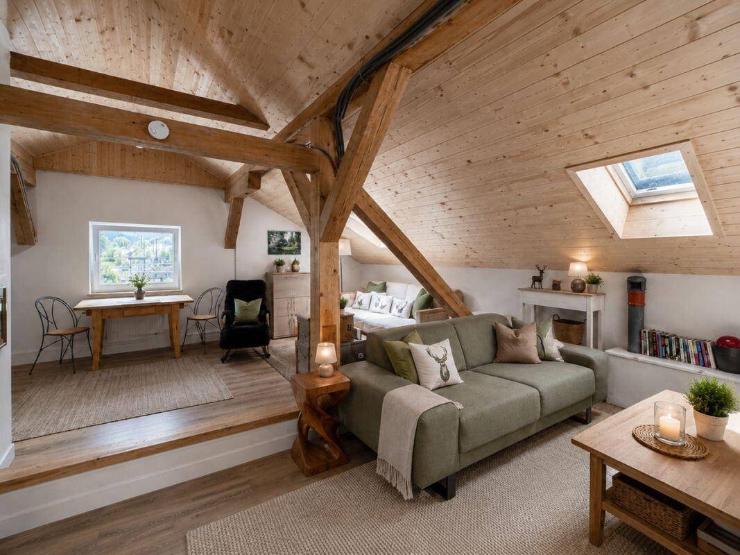 Helles Wohnzimmer im Dachgeschoss mit Holzbalken, Dachfenster und gemütlicher Einrichtung.