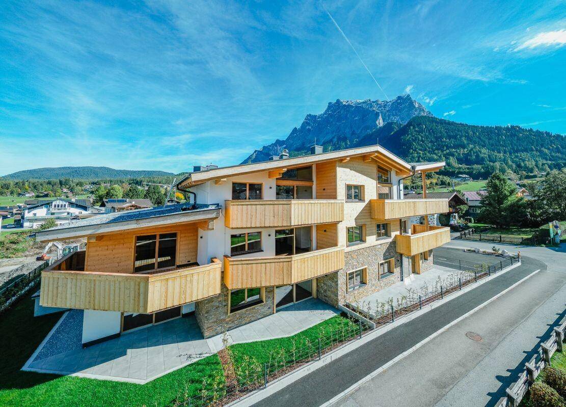 Moderne Wohnanlage mit Holzfassade und großzügigen Balkonen, harmonisch in die Bergwelt integriert.
