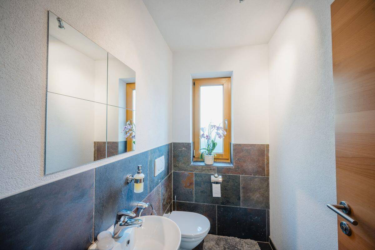 Helles Gäste-WC mit Fenster, modernem Waschbecken und dunklen Wandfliesen.