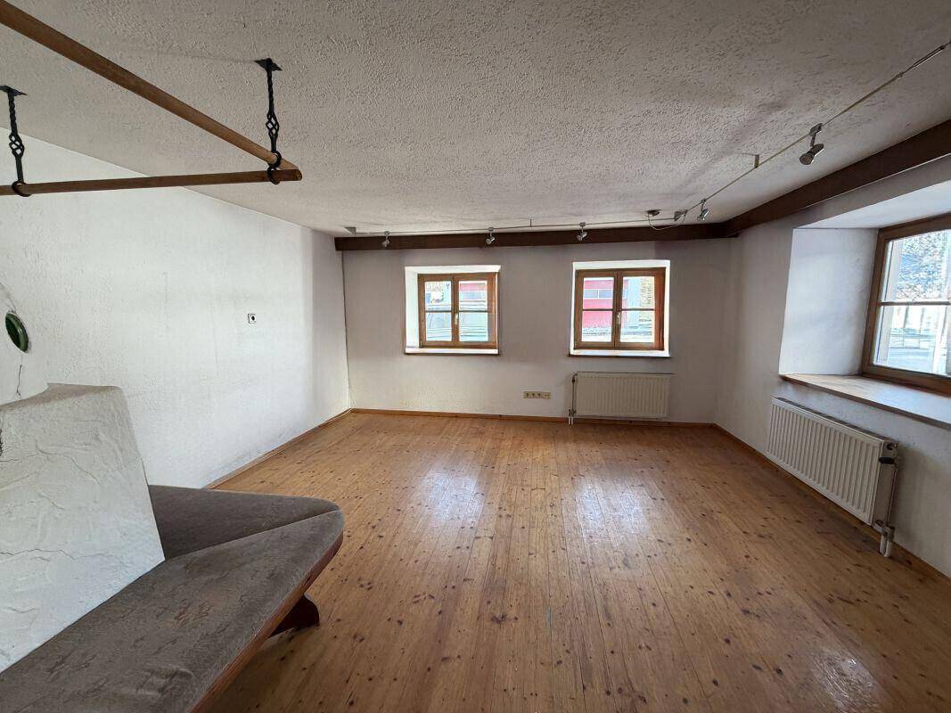 Heller, leerer Raum mit breiten Holzplankenböden, weißen Wänden und traditionellen Holzfenstern.