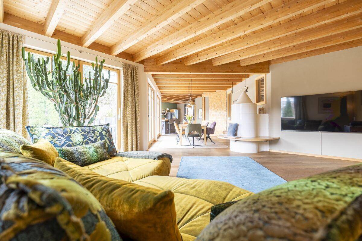 Gemütliches Wohnzimmer mit Holzbalkendecke, bequemer Couch und Blick ins Grüne.
