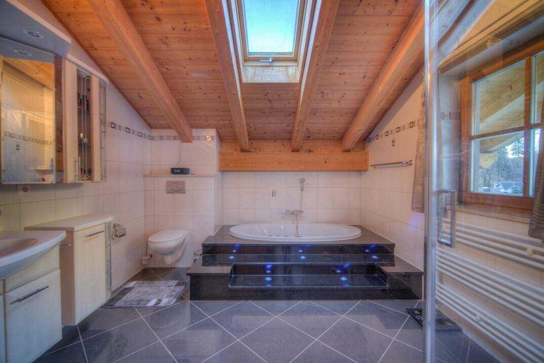 Geräumiges Badezimmer im Dachgeschoss mit Badewanne, Dachfenster und Holzbalken.