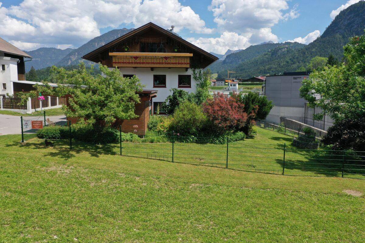 Gepflegter Garten mit Rasenfläche und Blick auf das Haus mit Holzbalkon und Bergpanorama.