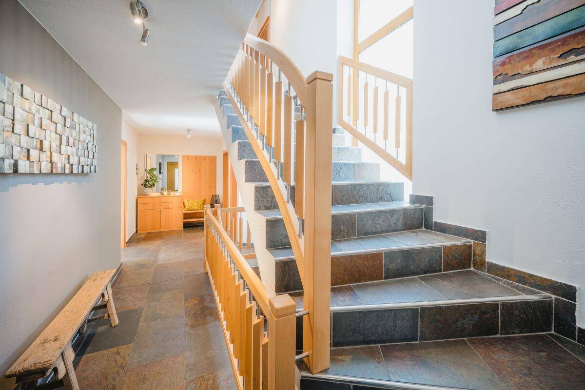 Heller Flur mit Natursteinfliesen und Holztreppe, die zu den oberen Etagen führt.