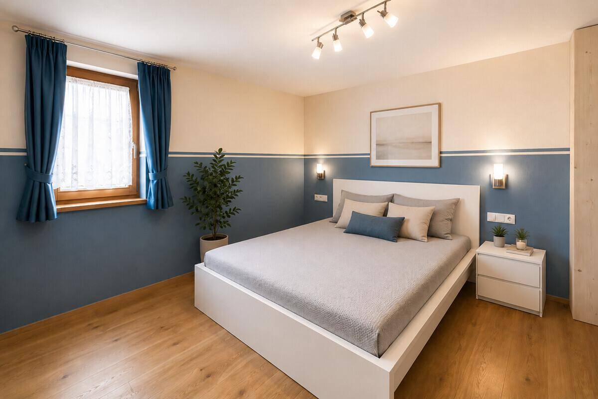 Modernes Schlafzimmer mit weißem Bett, zweifarbigen Wänden und blauen Vorhängen am Fenster.