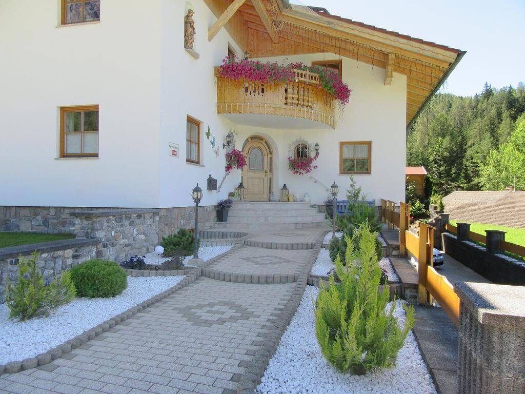 Eingangsbereich des Hauses mit gepflastertem Weg, Blumen und traditionellem Holzbalkon.