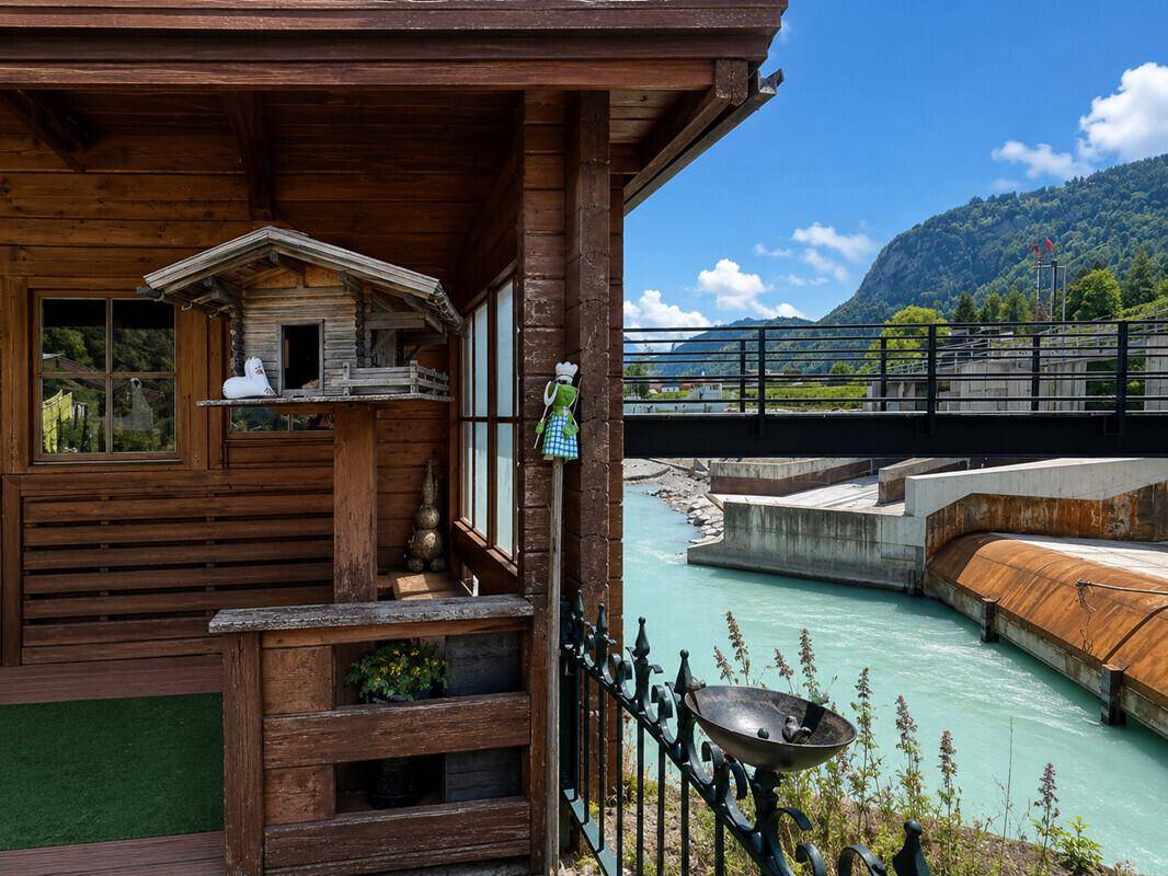 Detailansicht eines Holzhauses mit Vogelhäuschen und Blick auf den türkisfarbenen Fluss.