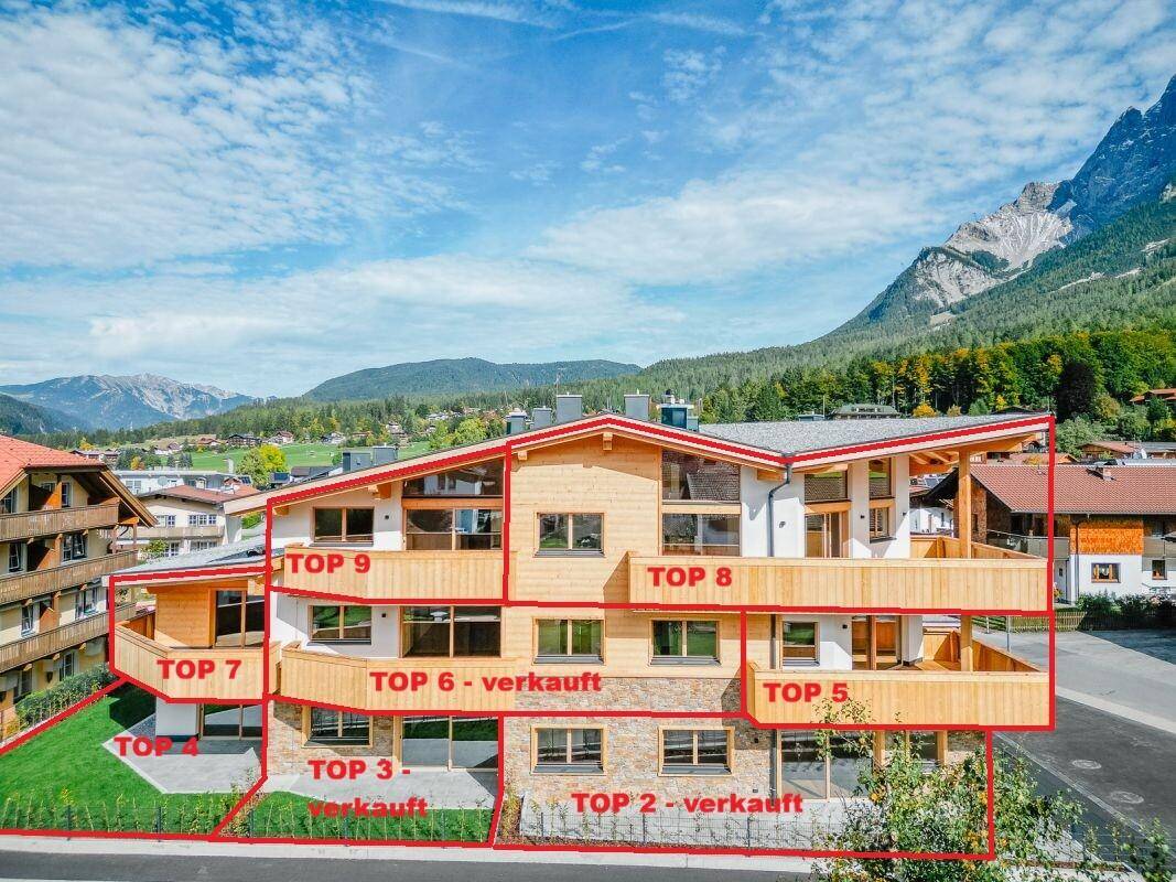 Übersicht des Gebäudes mit markierten Wohneinheiten und Verkaufsstatus vor Bergkulisse.