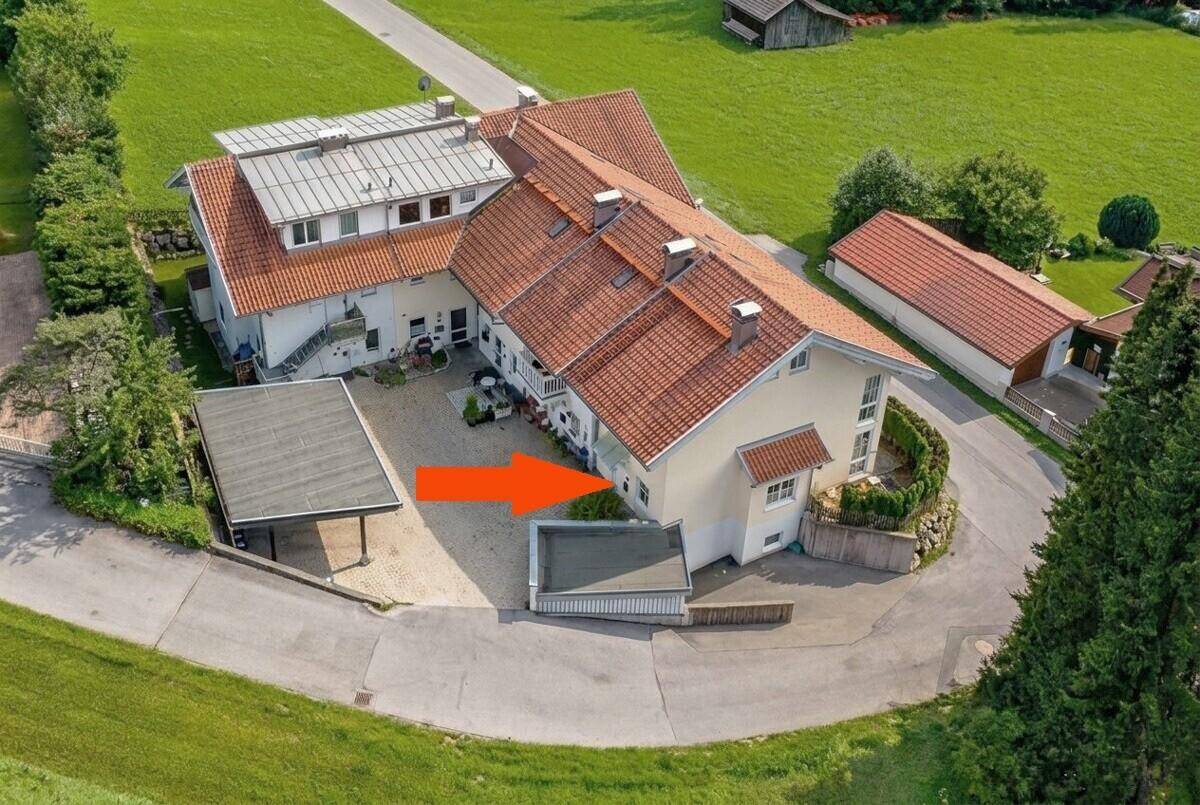 Luftaufnahme eines Mehrfamilienhauses mit umliegender Grünfläche und Parkplätzen in ländlicher Umgebung.