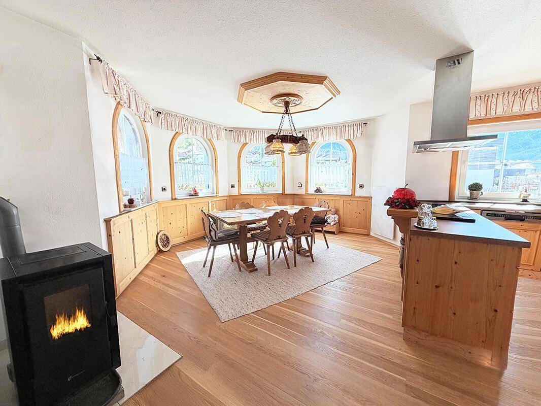 Gemütlicher Wohn-Essbereich im Landhausstil mit Holzboden, Kaminofen und Rundbogenfenstern.