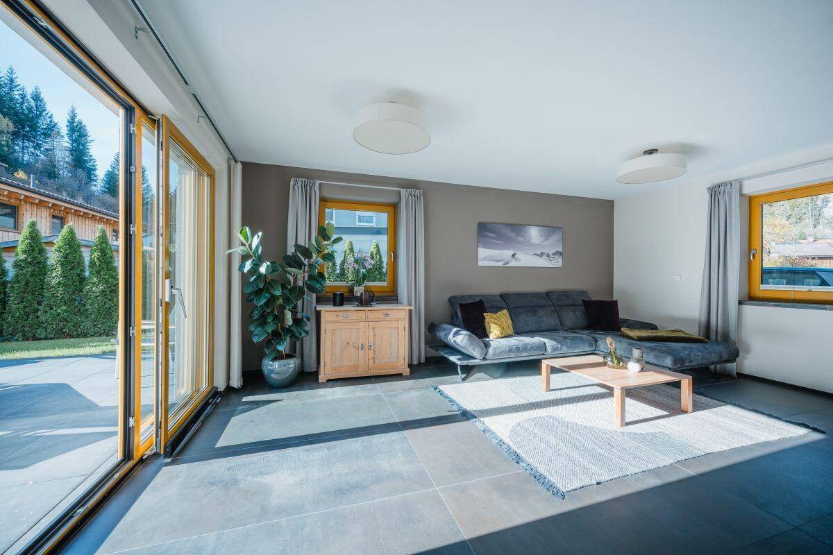 Helles Wohnzimmer mit großzügigen Glasfronten, modernem Sofa und dunklem Fliesenboden.