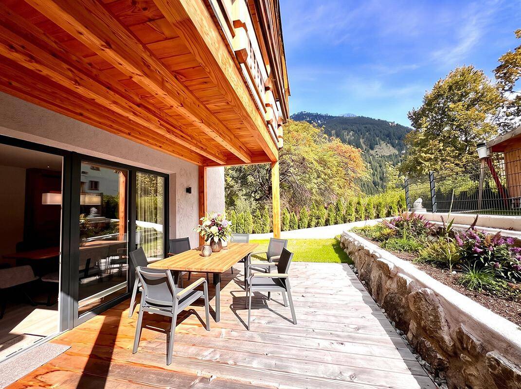 Geräumige Holzterrasse mit Esstisch und Stühlen, bietet einen schönen Blick auf die umliegende Berglandschaft.