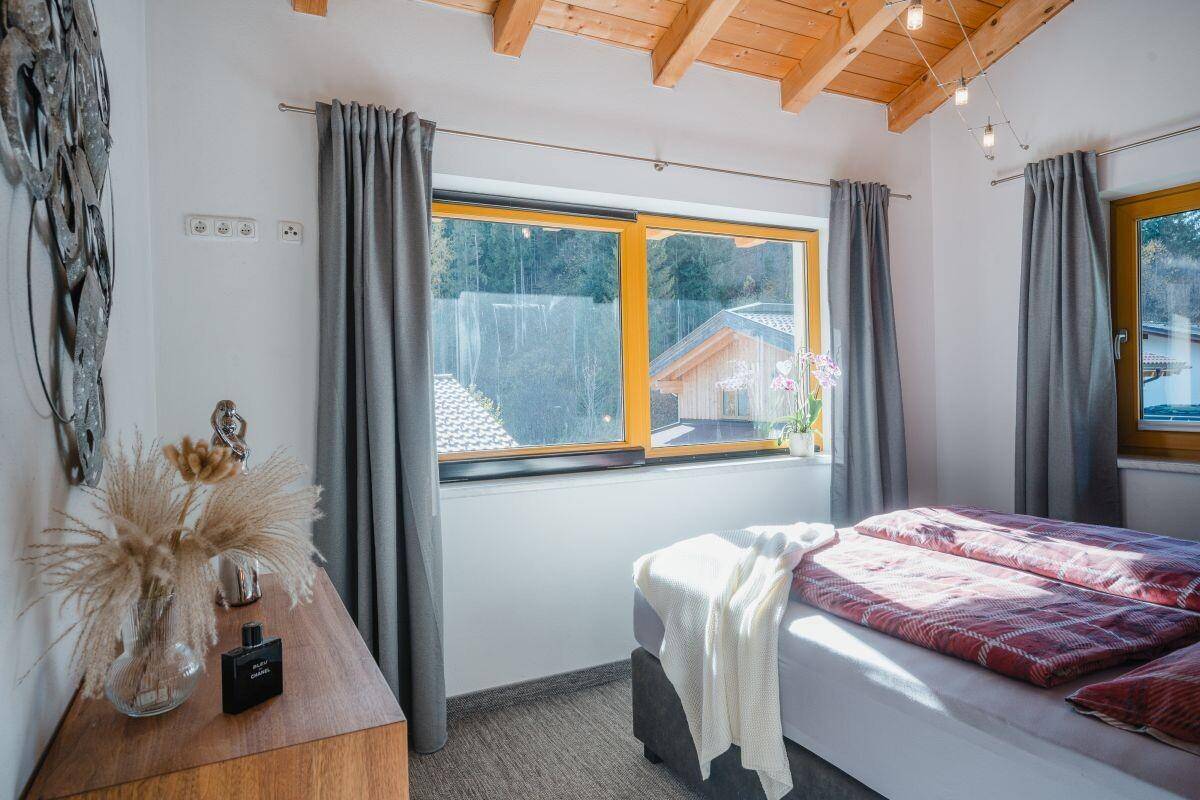 Gemütliches Schlafzimmer mit Holzbalkendecke, großem Fenster und Blick ins Grüne.