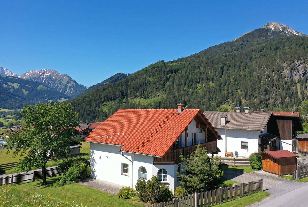 Rückansicht eines charmanten Hauses mit rotem Ziegeldach und grüner Umgebung.