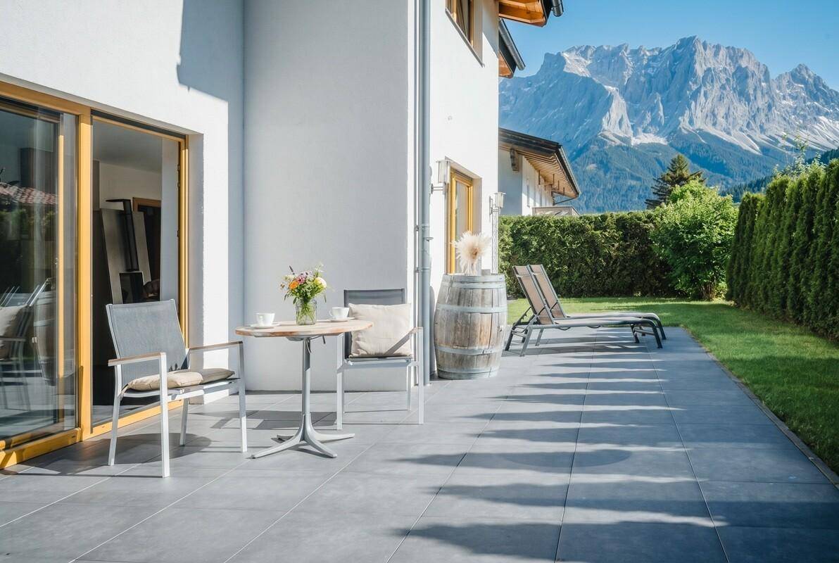 Geräumige Sonnenterrasse mit Liegestühlen und direktem Zugang zum Garten, umgeben von Bergen.