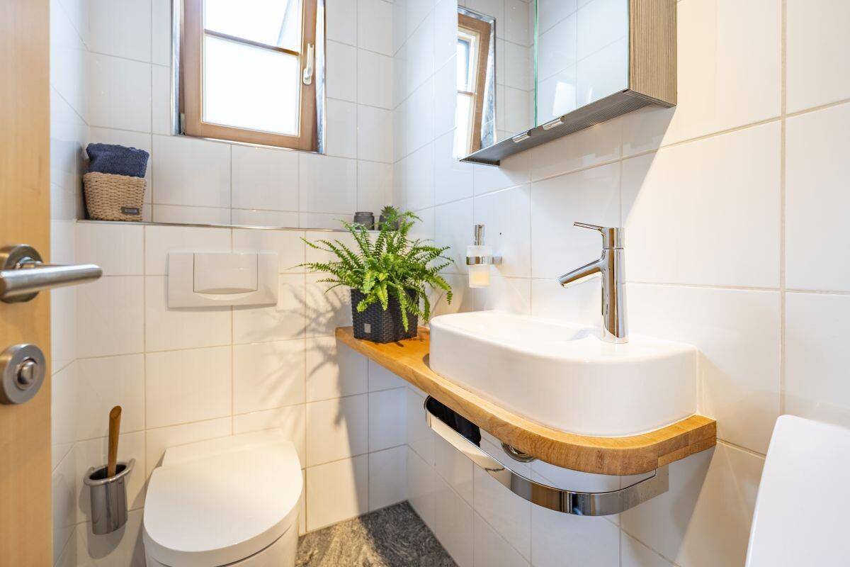 Kleines Gäste-WC mit modernem Waschbecken, Wand-WC und Fenster.