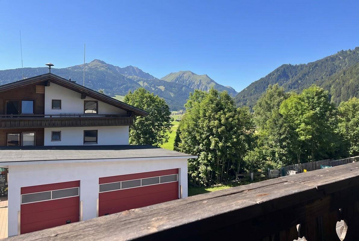 Weitläufiger Blick auf grüne Hügel, Bäume und ferne Berge, mit einem Garagengebäude im Vordergrund.