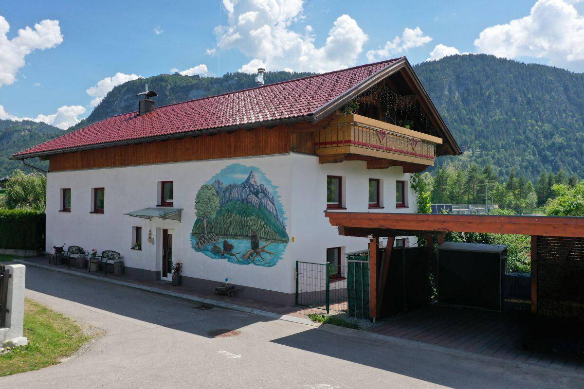 Traditionelles Haus mit Bergblick und Carport, umgeben von grüner Natur.
