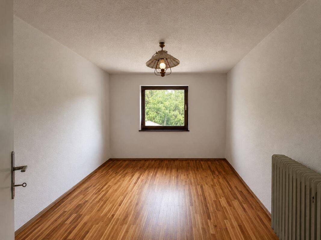 Leeres Zimmer mit Holzparkettboden und einem Fenster mit Blick ins Grüne, ideal für ein Schlafzimmer.
