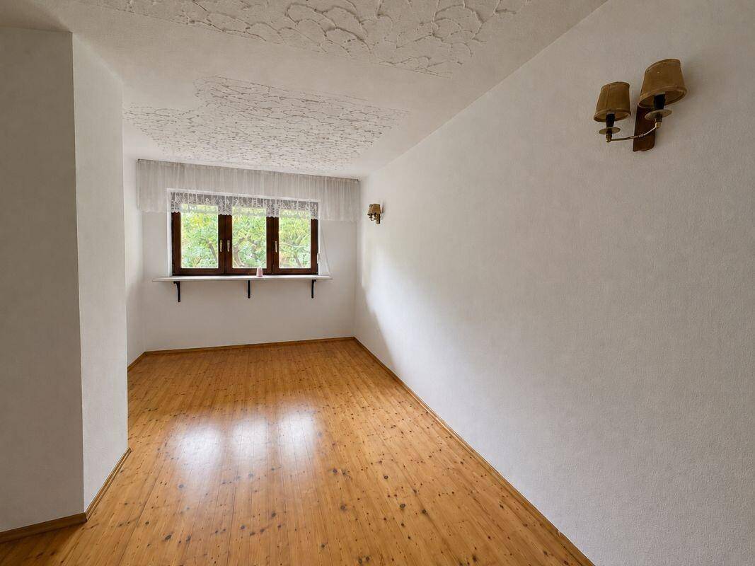 Helles Zimmer mit Holzparkettboden und strukturiertem Deckenputz, bereit zur individuellen Gestaltung.