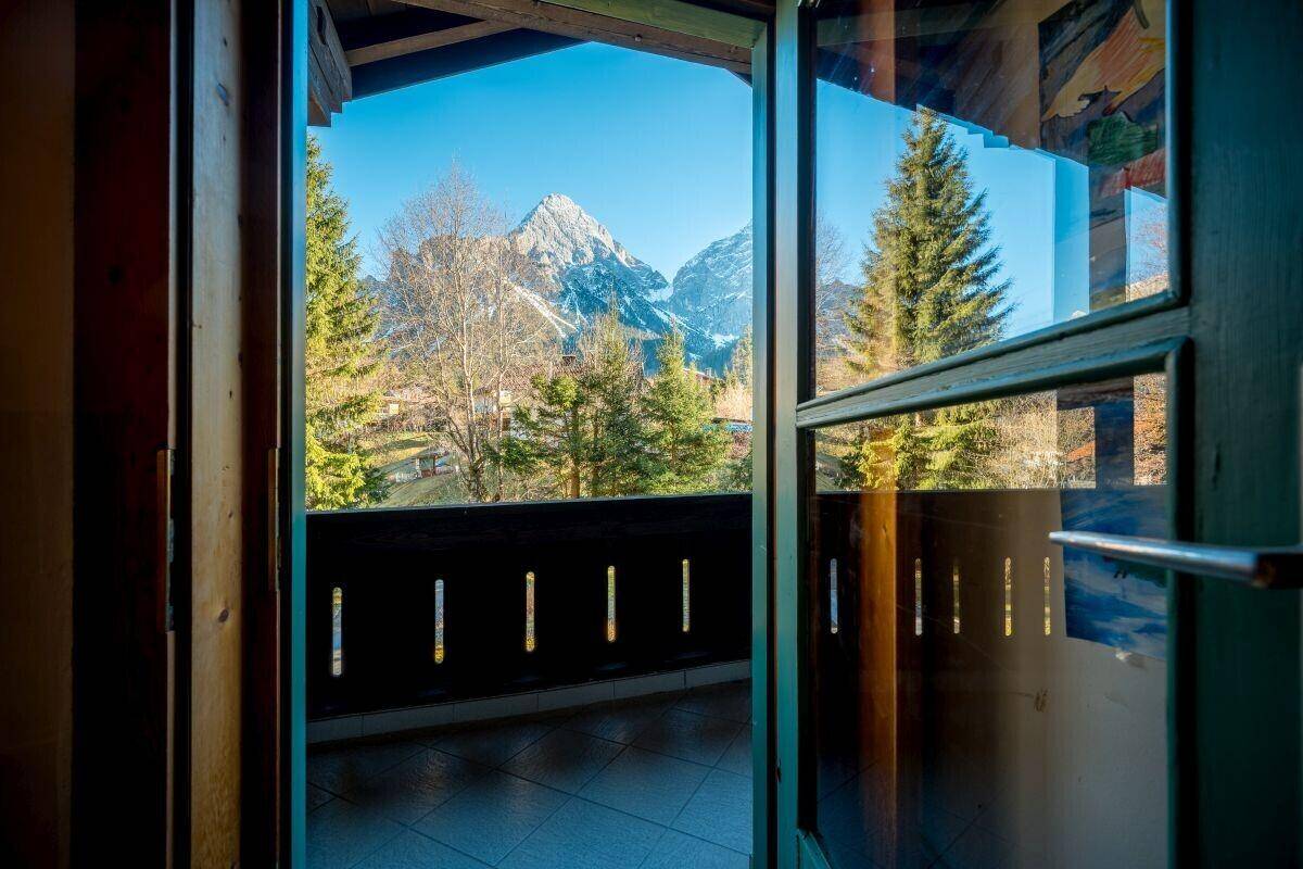 Blick durch die offene Balkontür auf die beeindruckende Bergwelt und grüne Natur.