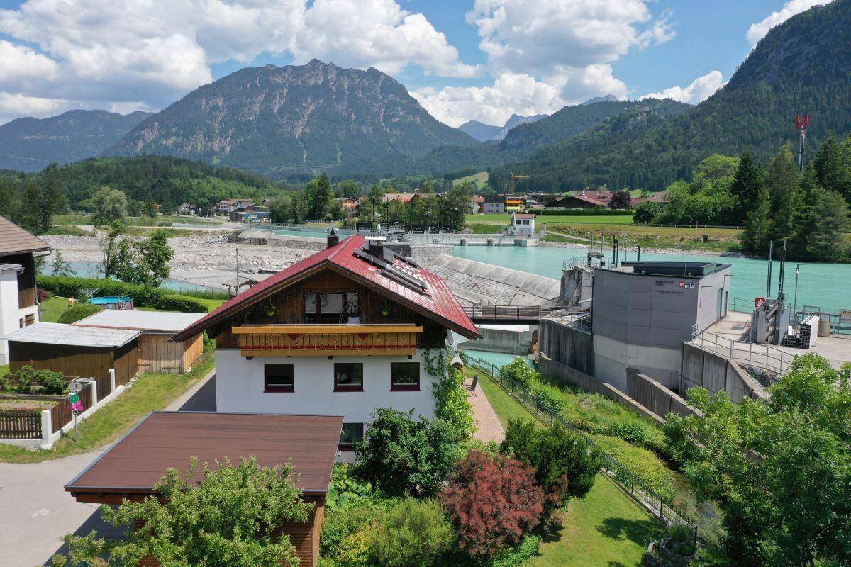 Anwesen mit rotem Dach und Solaranlage, umgeben von Natur und Flusslandschaft mit Bergen.