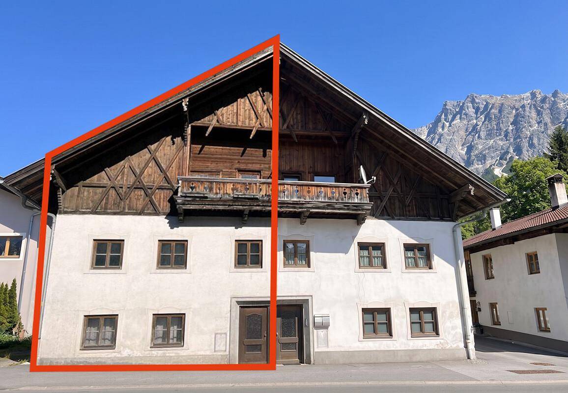 Traditionelles alpines Gebäude mit markanter Holzfassade und weißem Putz, umrahmt von einer roten Linie.