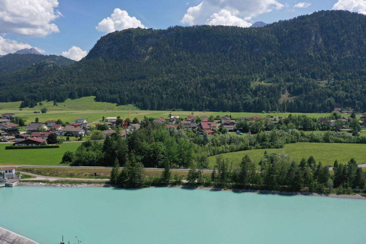 Idyllische Dorfansicht am Flussufer, umgeben von grünen Wäldern und Bergen.