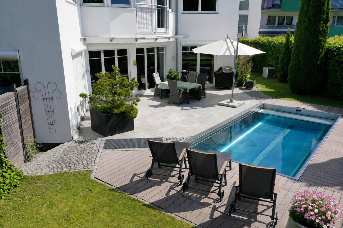 Sonniger Garten mit Swimmingpool, Liegestühlen und einer möblierten Terrasse am Haus.