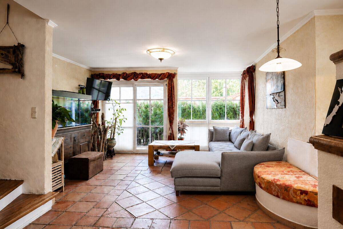 Gemütliches Wohnzimmer mit Terrakotta-Fliesenboden, bequemer Couch und großen Fenstern zum Garten.