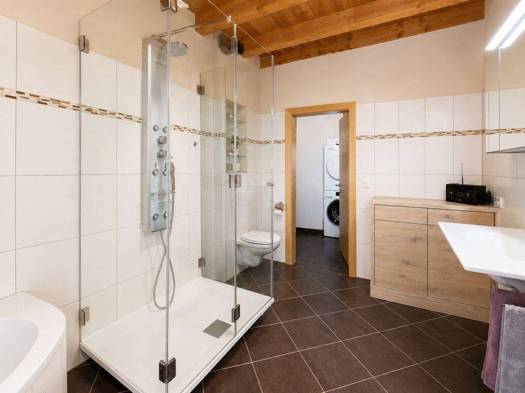 Modernes Badezimmer mit ebenerdiger Dusche, Eckbadewanne und Waschmaschinenanschluss.