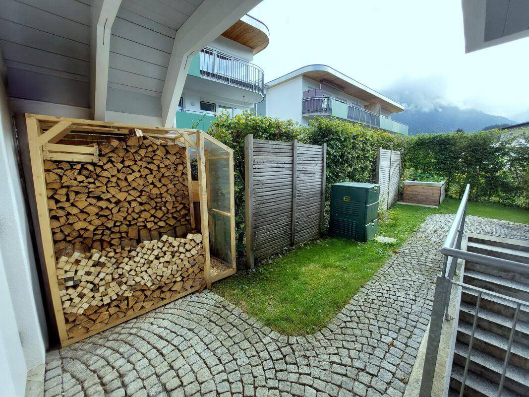 Lagerbereich im Garten mit gestapeltem Brennholz und Kompostbehältern.