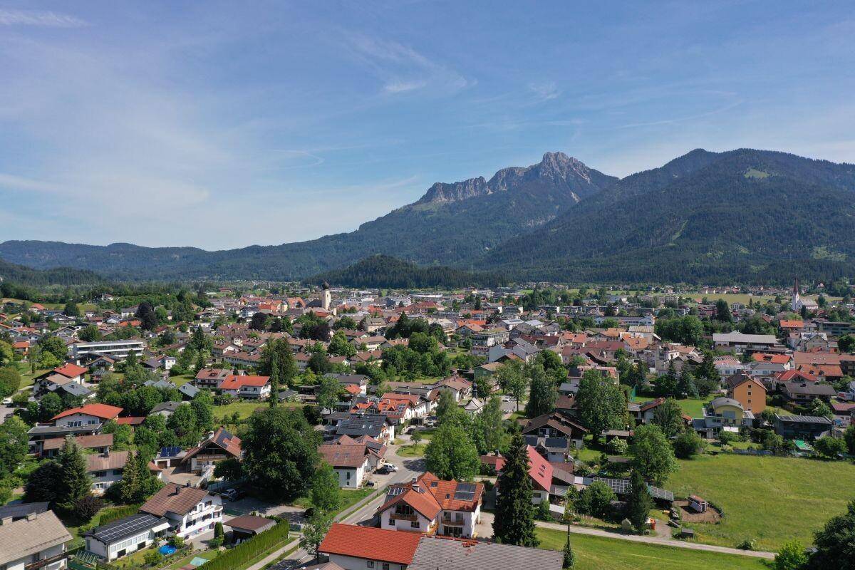 Luftaufnahme einer malerischen Stadt mit traditionellen Häusern, umgeben von grünen Feldern und majestätischen Bergen.