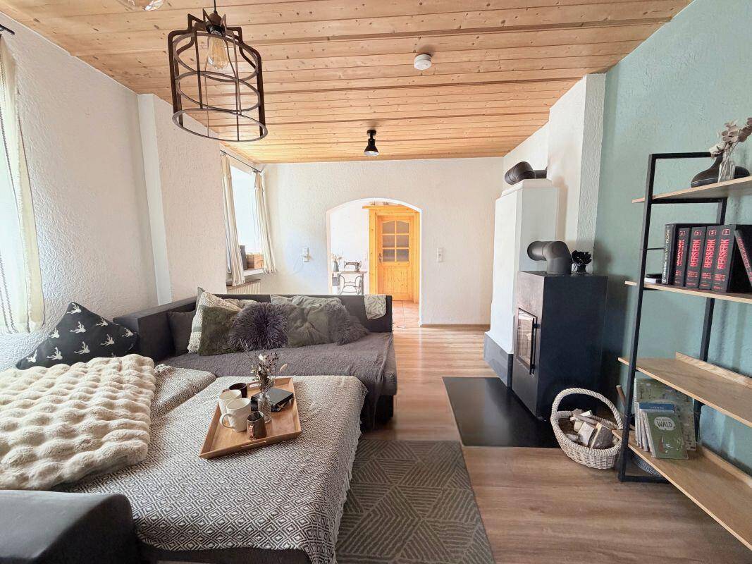 Geräumiges Wohnzimmer mit bequemer Couch, Holzbalkendecke und Durchgang zum Flur.