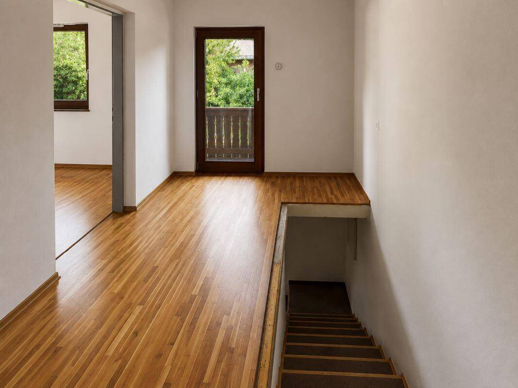 Heller Flur mit Holzparkettboden, Treppe und Zugang zu einem kleinen Balkon.