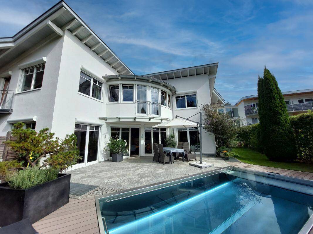 Elegante Hausfassade mit großzügiger Terrasse und integriertem Pool unter blauem Himmel.