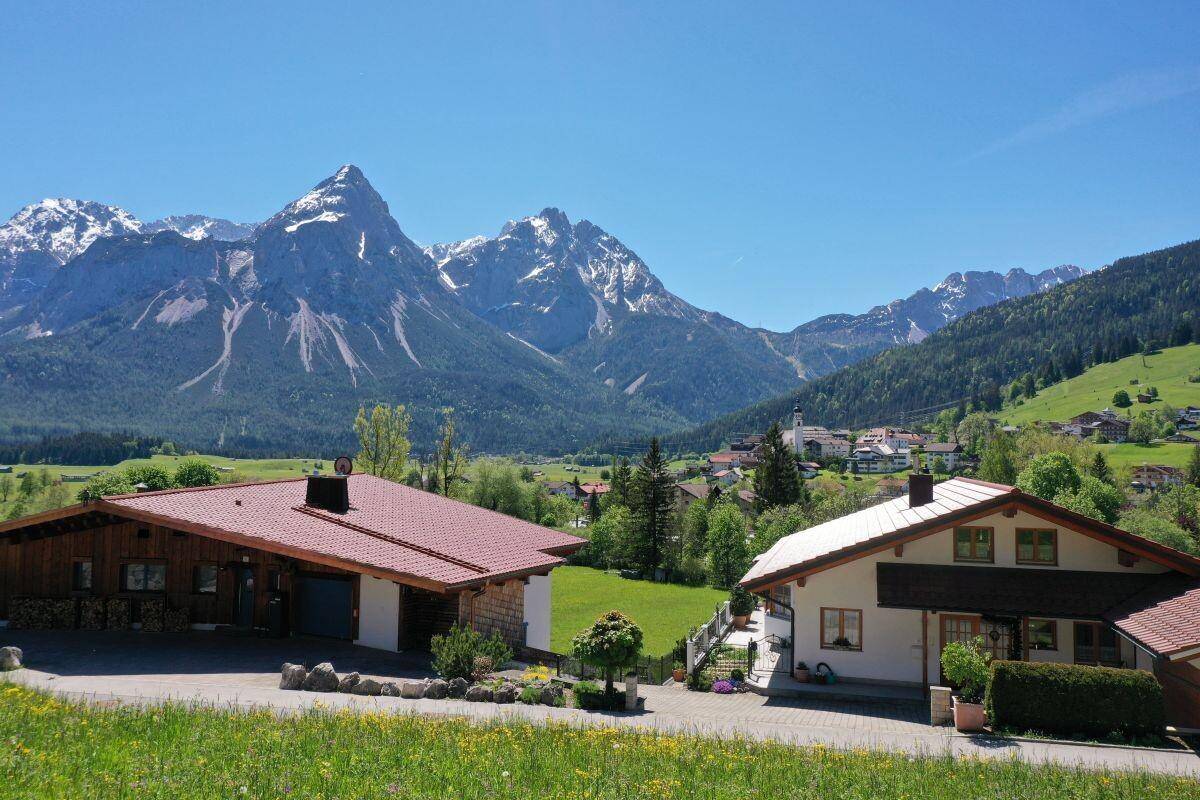Zwei traditionelle Häuser mit roten Ziegeldächern und gepflegtem Vorgarten vor einer Bergkulisse.