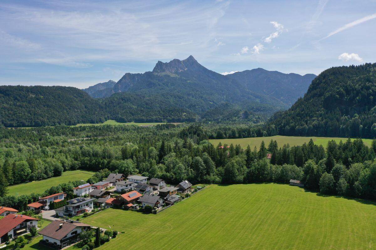 Luftaufnahme eines malerischen Dorfes eingebettet in eine grüne Landschaft mit majestätischen Bergen im Hintergrund.
